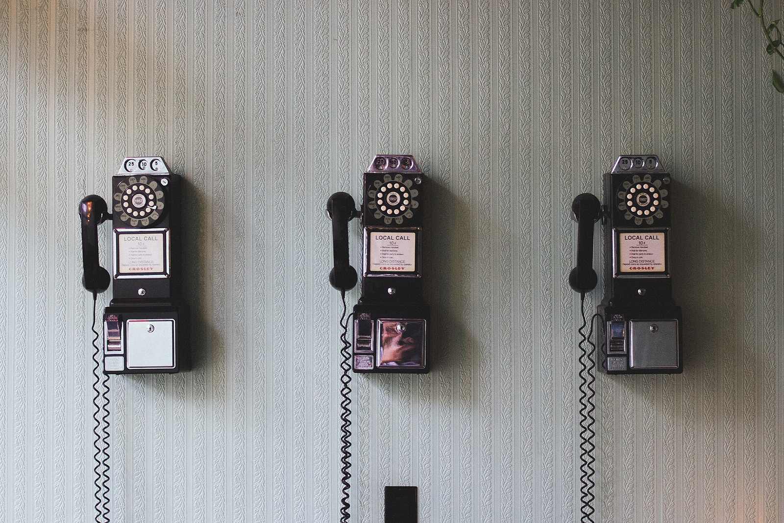 Three old pay telephones mounted on a pale wall